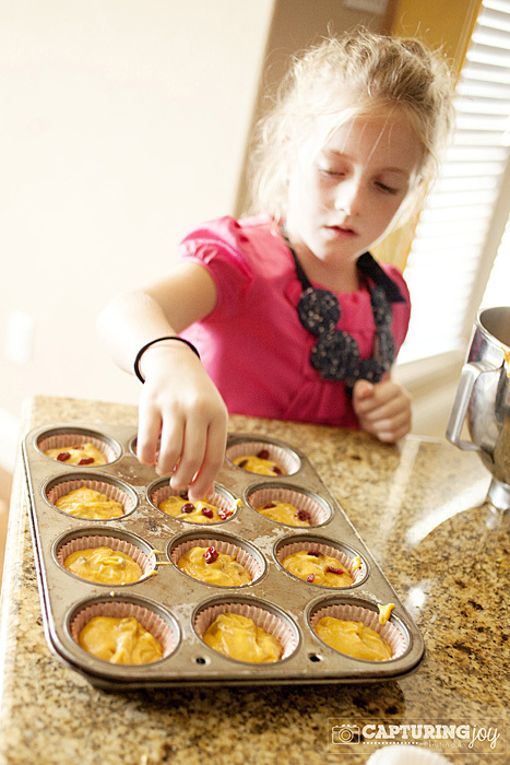 child adding cranberries to pumpkin cranberry muffins